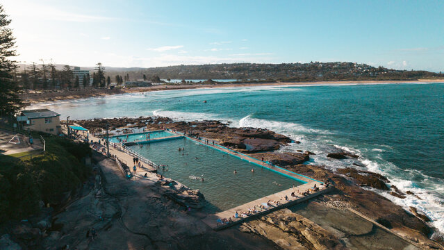 Aerial view of Dee Why Rock Pool with swimmers in the water, rocky coastline, and waves crashing against the shore in Dee Why, New South Wales, Australia.