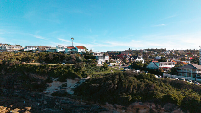 Aerial view of the coastal residential area with houses perched on the hillside overlooking the rocky coastline and lush greenery in Dee Why, New South Wales, Australia.