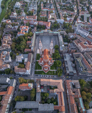 Aerial view of the Votive Church of Szeged with its twin towers and red roof, situated in the historic Dom ter surrounded by urban buildings and greenery in Szeged, Hungary.