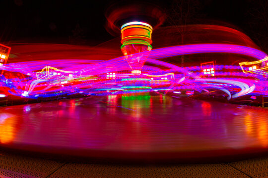 View of a spinning fairground ride at night captured with long exposure creating vibrant purple and red light trails in Almere, Flevoland, Netherlands.