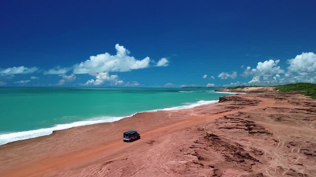 Aerial view of a vehicle driving along the red cliffs overlooking the turquoise ocean at Pipa Beach, State of Rio Grande do Norte, Brazil.