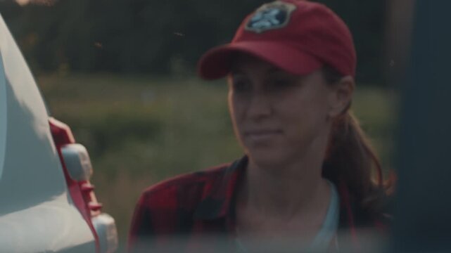 Young woman stands by the big 4x4 off road car and watches sunset in the wild and returns into the car
