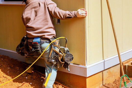 Worker is fastening wall panels to building frame at construction site with nail gun tools equipment