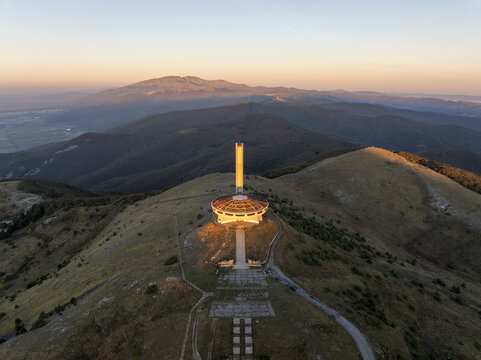 Aerial view of the Buzludzha Monument on a mountain peak at sunset with surrounding hills and landscape in Stara Zagora, Bulgaria.