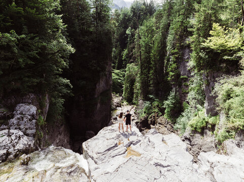 Aerial view of a couple standing on a rock ledge overlooking the Aubachfall waterfall in a deep forested gorge in Hallein, Salzburg, Austria.