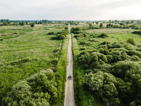 Aerial view of a lone cyclist on a dirt path through a lush green landscape with bushes and trees in Poland.