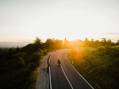 Aerial view of a cyclist bikepacking along a winding road through the rolling hills of Tuscany, Italy.