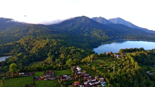 Aerial view of Jalan Raya Wanagiri overlooking the lush green mountains and the serene lake surrounded by dense tropical forest in Kecamatan Sukasada, Bali, Indonesia.