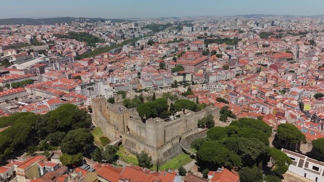 Aerial view of Castelo de Sao Jorge surrounded by historic city rooftops and lush trees in Lisbon, Portugal.