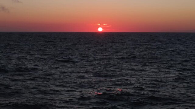 Aerial view of sunset over the Baltic Sea with calm dark waves reflecting the red light of the sun in Palanga, Klaipeda County, Lithuania.