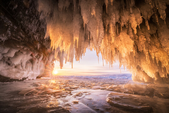 View of the frozen ice cave at Lake Baikal with hanging icicles illuminated by the golden sunrise in Irkutsk, Irkutsk Oblast, Russia.