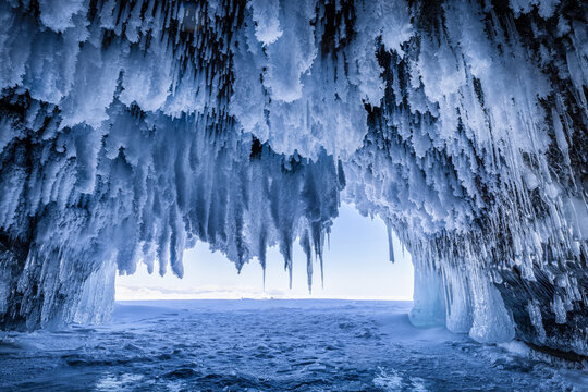 View of the frozen ice cave at Lake Baikal with intricate icicles hanging from the ceiling and a vast expanse of ice in Irkutsk, Irkutsk Oblast, Russia.