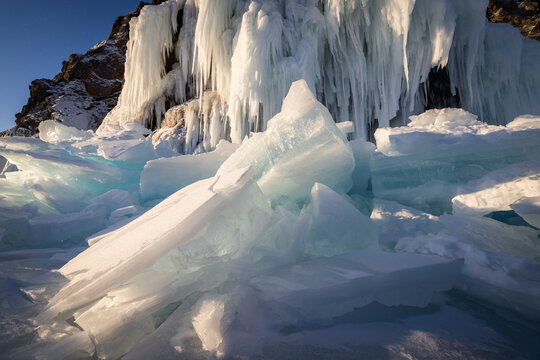 View of Lake Baikal featuring massive ice formations and large icicles hanging from rocky cliffs under clear winter light in Irkutsk, Irkutsk Oblast, Russia.