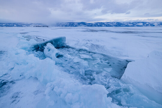 View of the frozen surface of Lake Baikal with jagged ice ridges and snow under a cloudy winter sky in Irkutsk, Irkutsk Oblast, Russia.
