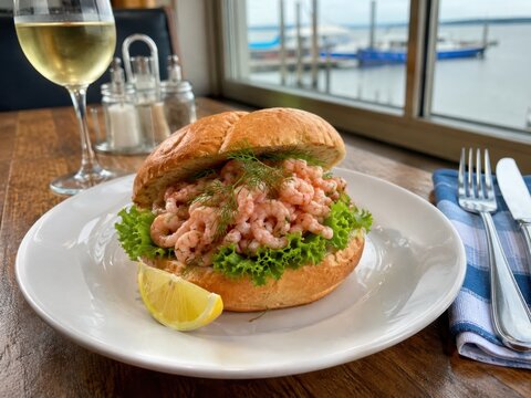 Krabbenbr&ouml;tchen im deutschen Restaurant: Frisches Br&ouml;tchen mit Nordseekrabben, Blattsalat, Dill und Zitrone, serviert als norddeutscher Klassiker mit Blick aufs Wasser.