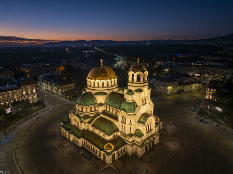 Aerial view of Patriarchal Cathedral St. Alexander Nevsky illuminated at twilight with golden domes and green roofs in Sofia, Sofia City Province, Bulgaria.