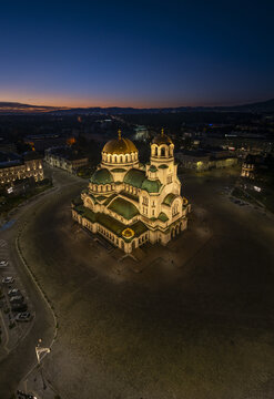 Aerial view of the illuminated Patriarchal Cathedral St. Alexander Nevsky at night, surrounded by the city square and urban lights in Sofia, Sofia City Province, Bulgaria.