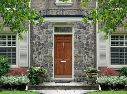 Elegant wood grain front door of traditional two story house with shutters around windows