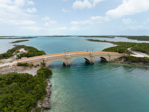 Aerial view of Crab Cay Bridge spanning turquoise waters with lush tropical vegetation and a clear blue sky in Exuma, The Bahamas.
