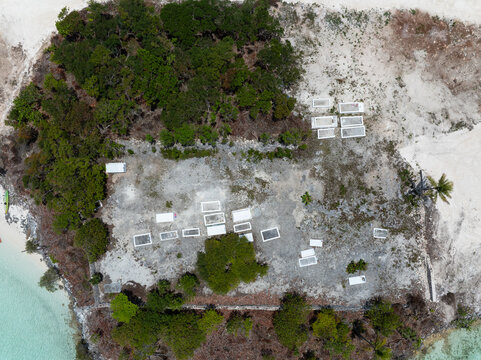 Aerial view of a historic cemetery with white grave markers scattered across rocky terrain, surrounded by lush green trees and vegetation near the coastline in Exuma, Bahamas.