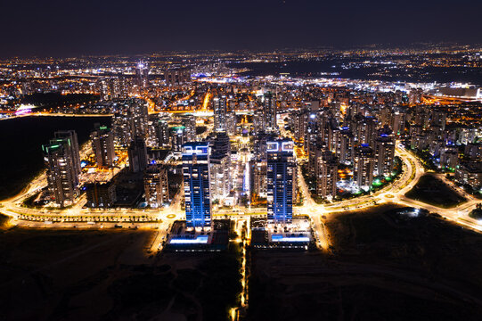 Aerial view of the illuminated skyline of Netanya at night, featuring modern skyscrapers, glowing city streets, and urban infrastructure in Netanya, Center District, Israel.