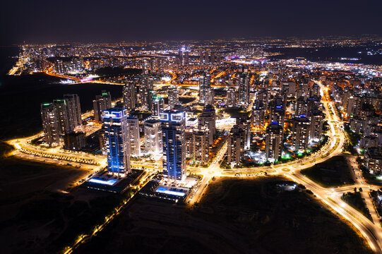 Aerial view of the illuminated cityscape of Netanya at night, featuring modern high-rise residential towers, glowing street lights, and urban infrastructure in Netanya, Center District, Israel.