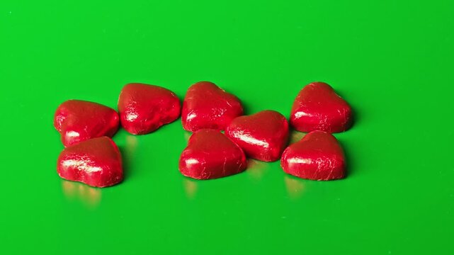 Heart shaped chocolates arranged on green background in different groups