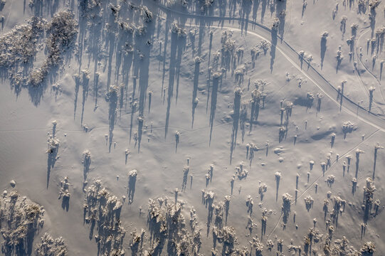 Aerial view of Gaustablikk Fjellresort area in winter, featuring snow-covered landscape with scattered pine trees casting long shadows, and a winding road in Rjukan, Telemark, Norway.