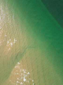 Aerial view of the coastal waters and sandy shoreline showing the contrast between the shallow golden sand and the deep green sea in Malahide, County Dublin, Ireland.