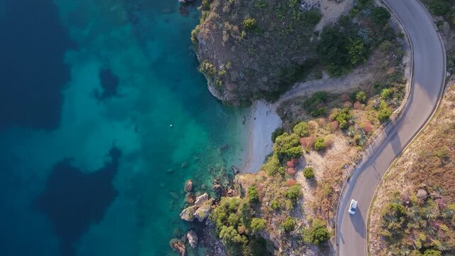 Aerial view of a car driving along a winding coastal road overlooking the turquoise waters of the Ionian Sea in Porto Palermo, Qarku i Vlores, Albania.