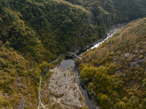 Aerial view of Devil's Bridge spanning the Arda River, surrounded by dense autumn forests and rocky slopes in Kardzhali Province, Bulgaria.