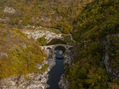 Aerial view of Devil's bridge spanning the Arda River surrounded by dense autumn forests in Kardzhali Province, Bulgaria.
