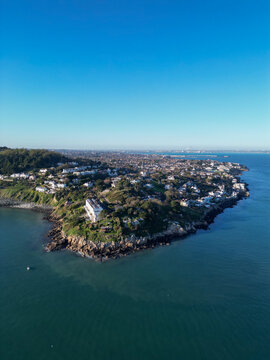 Aerial view of Dalkey coastline featuring rocky cliffs, residential houses, and the sea under a clear blue sky in Dublin, County Dublin, Ireland.