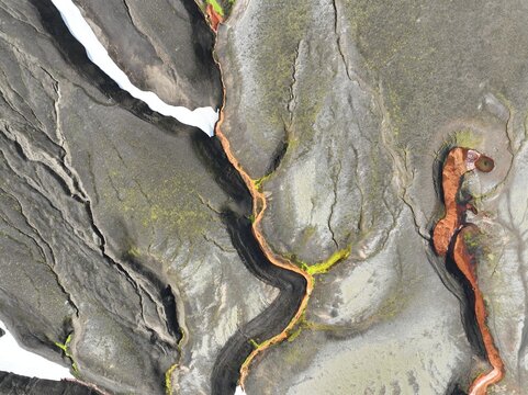 Aerial view of the volcanic landscape of Raudufossafjoll featuring dark basaltic terrain, vibrant orange mineral deposits, and patches of green moss in Hella, Rangarthing ytra, Iceland.
