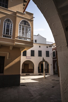View of the historic architecture and arched passageways of the old town square, featuring traditional stone buildings and sunlit cobblestone streets Ciutadella, Balearic Islands, Spain.