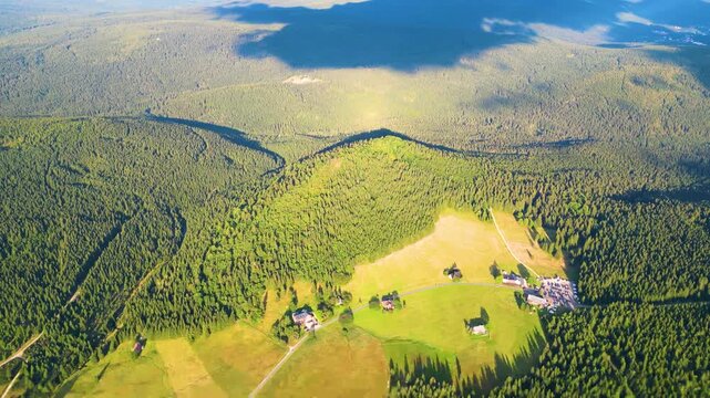 Aerial view of Bukovec Hill at Jizerka Village surrounded by dense coniferous forests and rolling green meadows in Korenov, Liberec Region, Czechia.