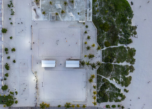 Aerial view of beach sports courts with people playing soccer and volleyball surrounded by palm trees and sand in Progreso, Yucatan, Mexico.