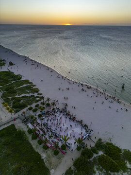 Aerial view of a pink basketball court on the beach with people gathering at sunset near the calm ocean in Progreso, Yucatan, Mexico.