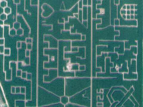 Aerial view of a large corn maze with intricate geometric patterns and shapes carved into the green fields in Soultz-Haut-Rhin, Grand Est, France.