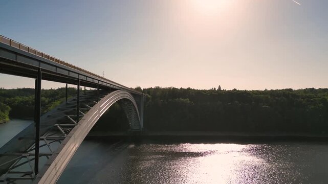 Aerial view of Zakov Bridge spanning the Vltava River, surrounded by lush forest under a bright sun in Orlik nad Vltavou, South Bohemian Region, Czechia.