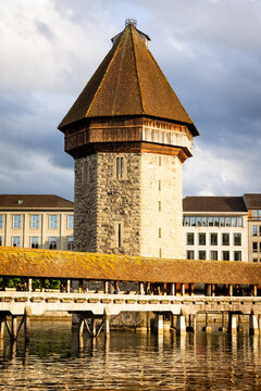 View of the historic Chapel Bridge and the octagonal Wasserturm stone tower spanning the Reuss river with people walking along the wooden structure in Lucerne, Lucerne, Switzerland.