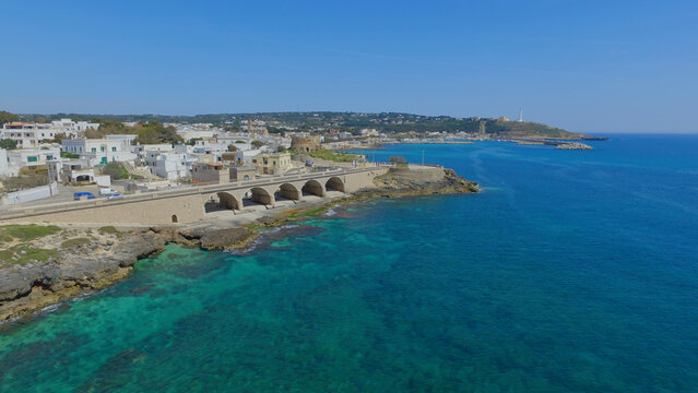 Aerial view of the historic stone bridge and white coastal architecture along the turquoise Ionian Sea in Santa Maria di Leuca, Puglia, Italy.