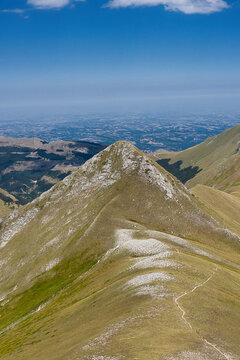 Aerial view of Pizzo Berro with its rocky peak and grassy slopes under a clear blue sky in Montefortino, Marche, Italy.