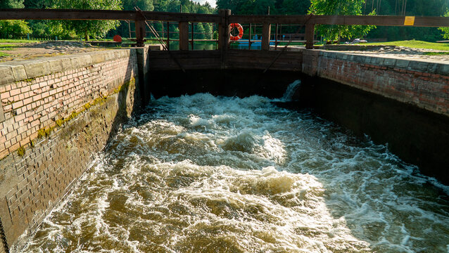 Water flowing through a lock with wooden gates near a river on a sunny day