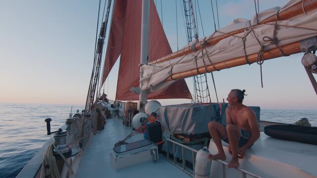 Sailing the Atlantic. Male sailor sits on the deck of the big sailing boat moving in the Atlantic Ocean under the sails and enjoys the last light of the day