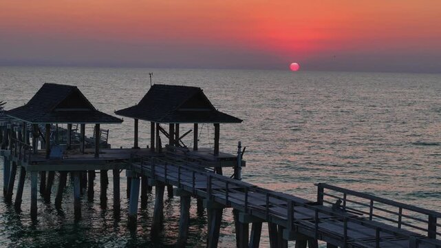 Aerial view of the historic Naples Pier extending into the Gulf of Mexico during a vibrant sunset with calm waters in Naples, Florida, United States.