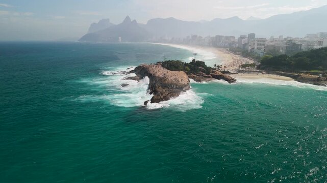 Aerial view of the Arpoador rock formation jutting into the turquoise Atlantic Ocean with the sandy Ipanema beach and coastal city skyline in Rio de Janeiro, Rio de Janeiro, Brazil.