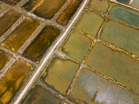 Aerial view of the salt pans in Quelfes, featuring rectangular basins with varying water colors and textures separated by narrow paths in Quelfes, Faro District, Portugal.