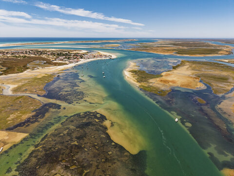 Aerial view of the Ria Formosa lagoon with winding tidal channels, sandbanks, and small boats near the coast of Quelfes, Faro District, Portugal.