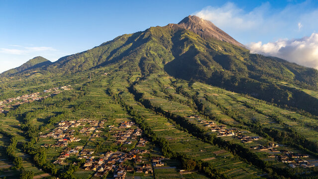 Aerial view of Mount Merapi towering over the terraced agricultural fields and village houses in Selo, Central Java, Indonesia.